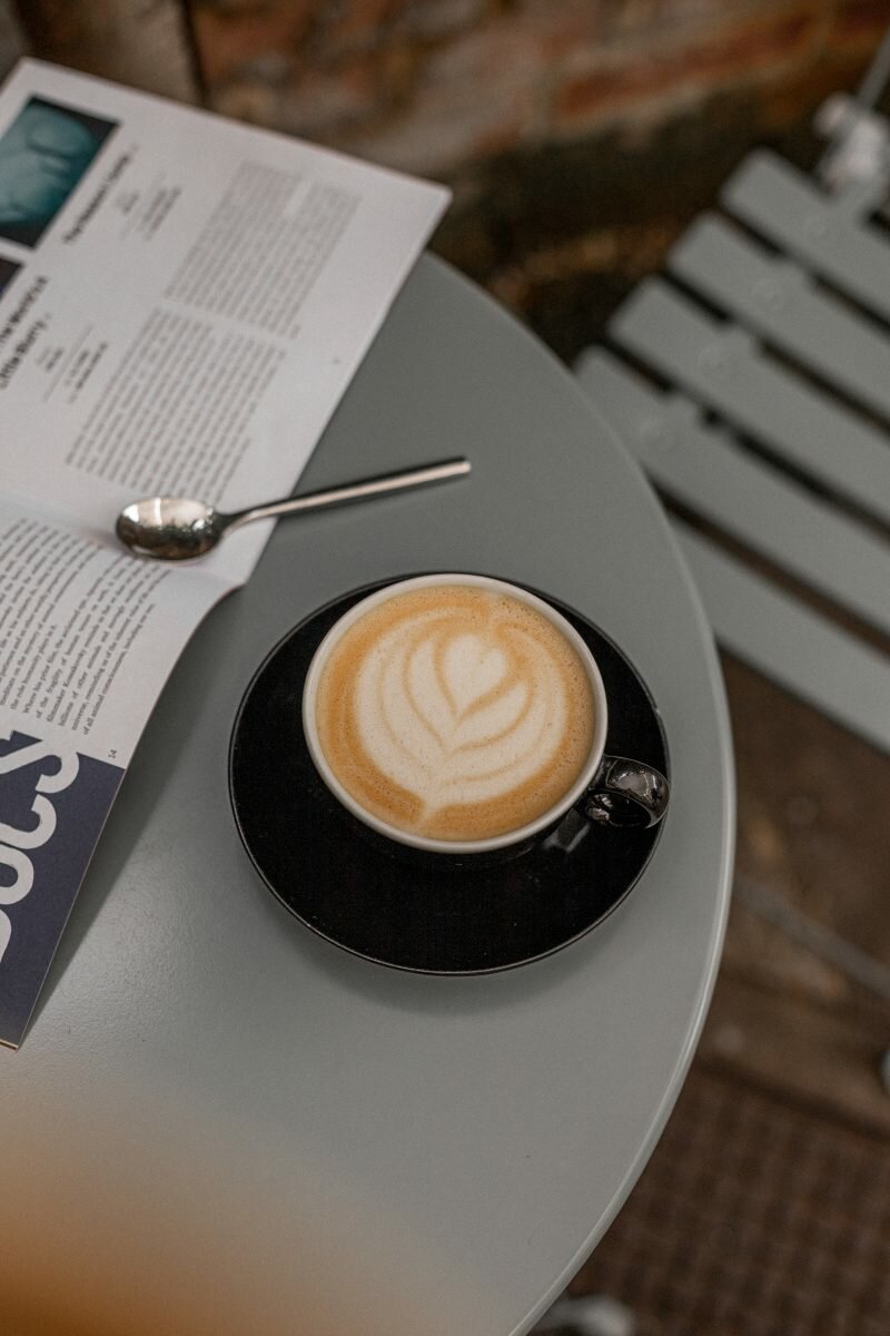 A black coffee cup containing a latte on a light blue table